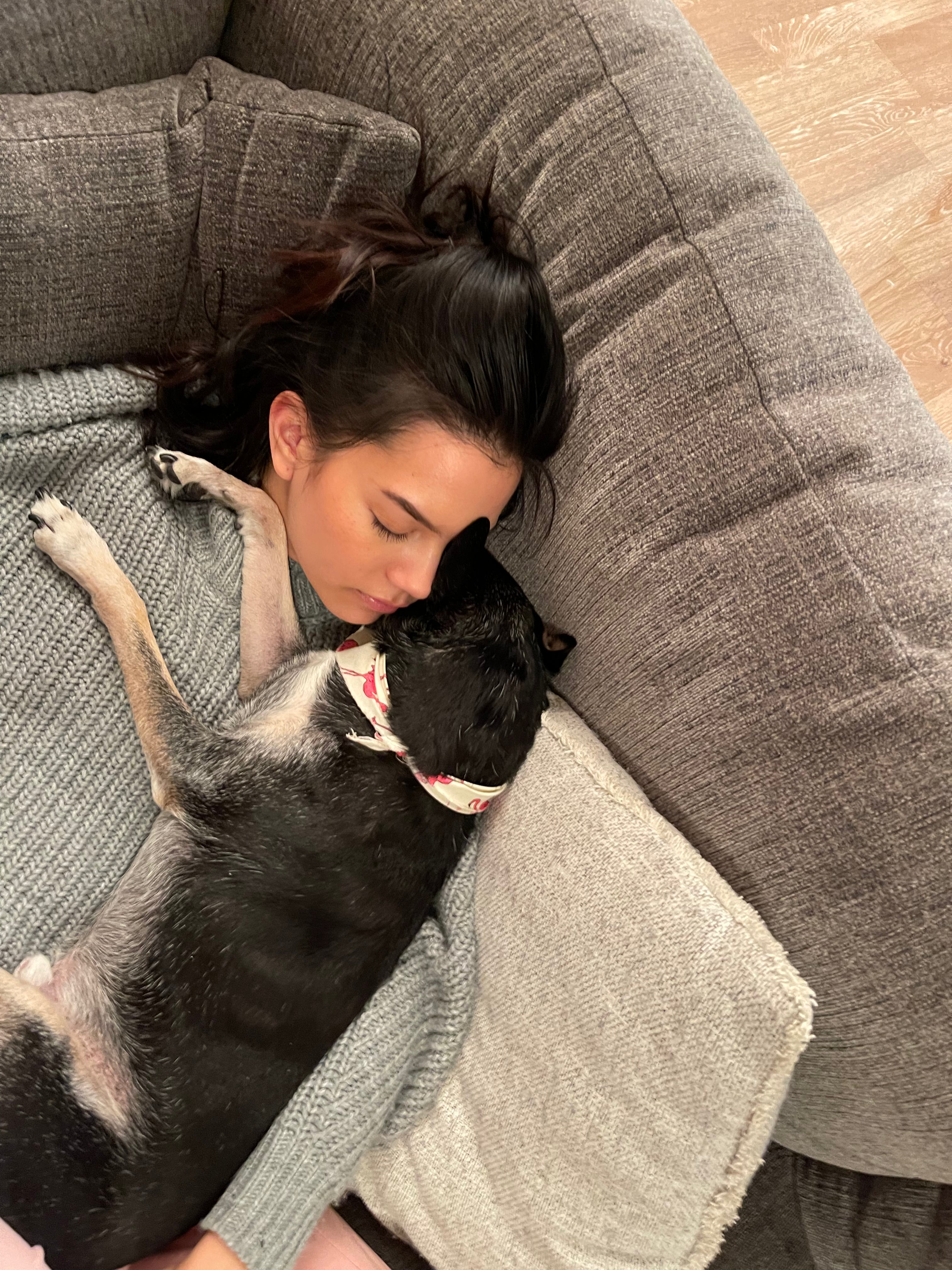 Woman lying on a gray couch with a black dog on her chest