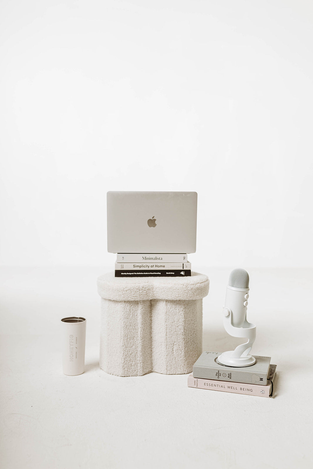 Laptop on a coral-like stand with books and a microphone on a white background