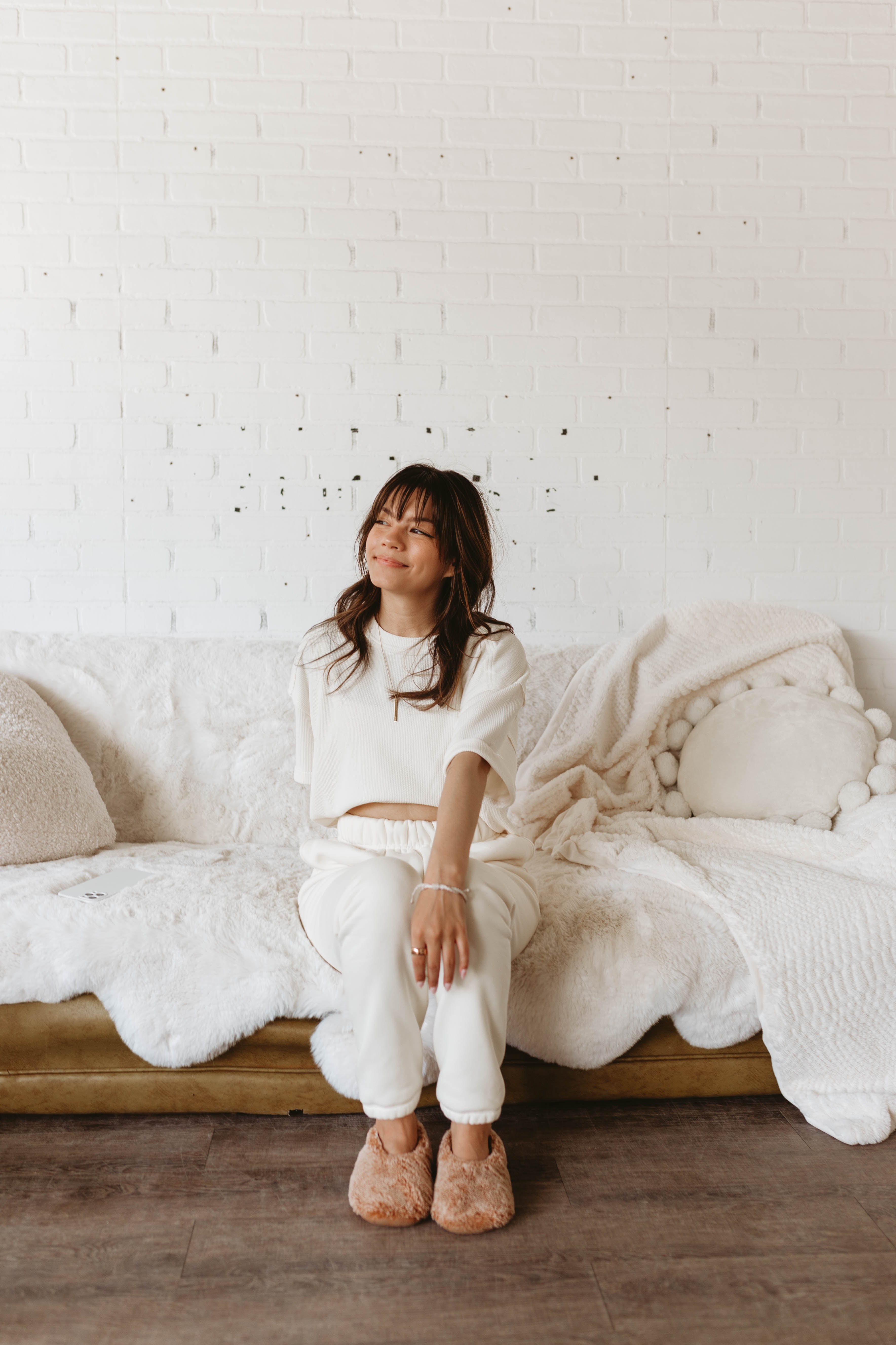 Woman sitting on a white couch in a room with a white brick wall.
