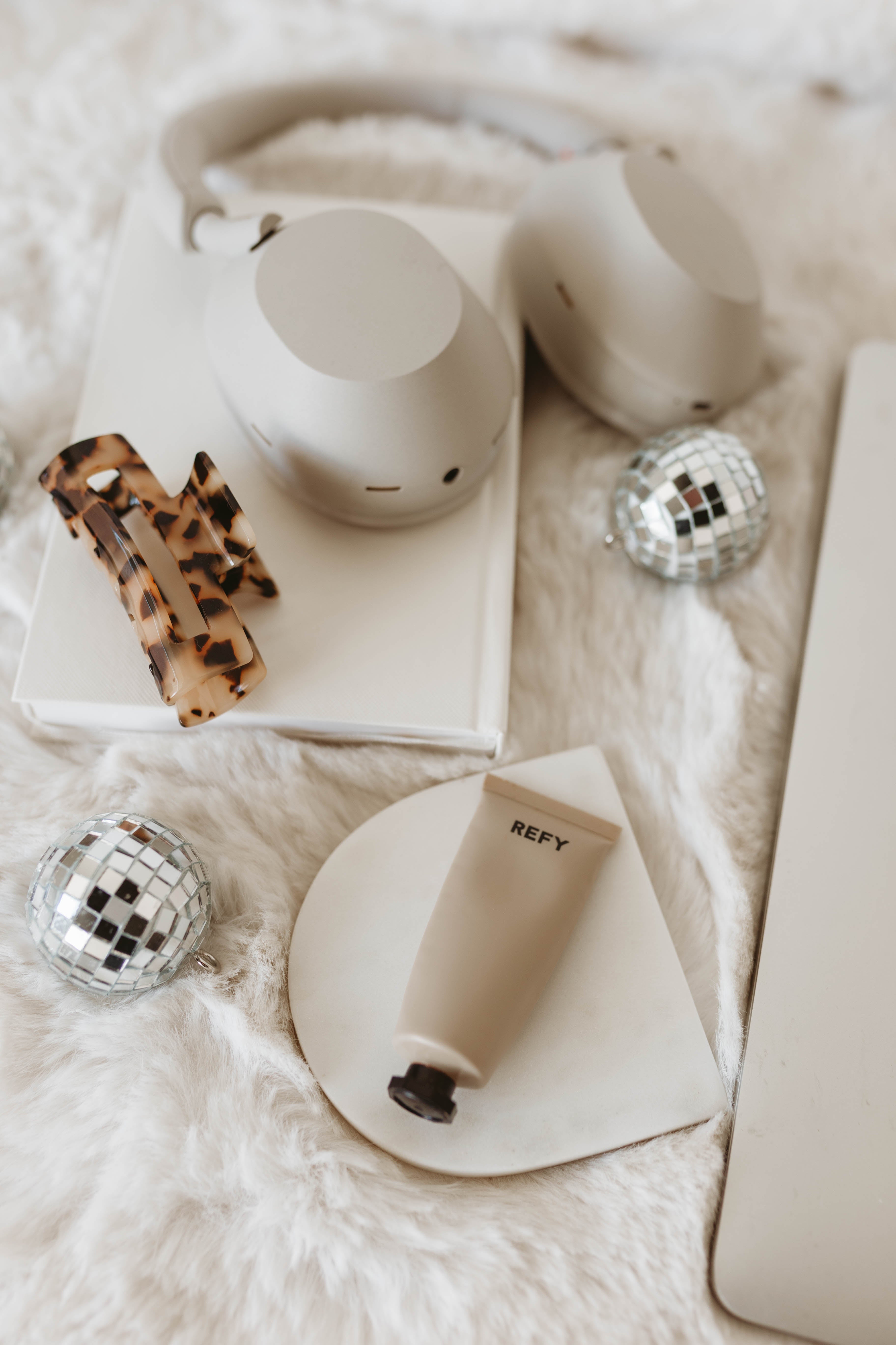 White mug, leopard print hair clip, disco balls, and beige tube of lip balm on a white surface.